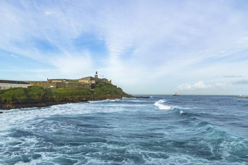 A boat leaving a port with a view of a historic fort on a hilltop.
