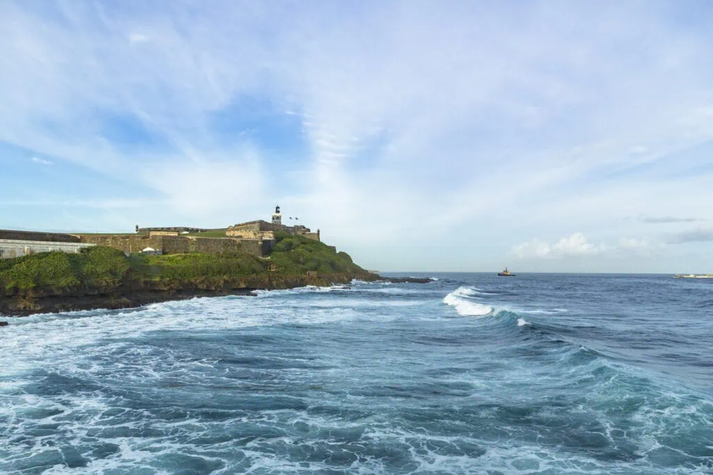 A boat leaving a port with a view of a historic fort on a hilltop.