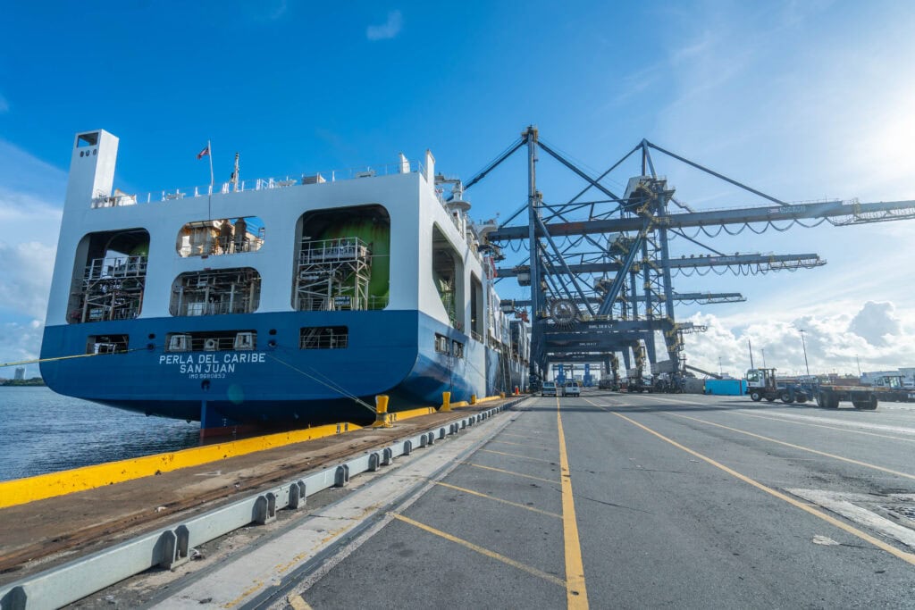Cargo ship docked at port in the Virgin Islands with cranes in the background.