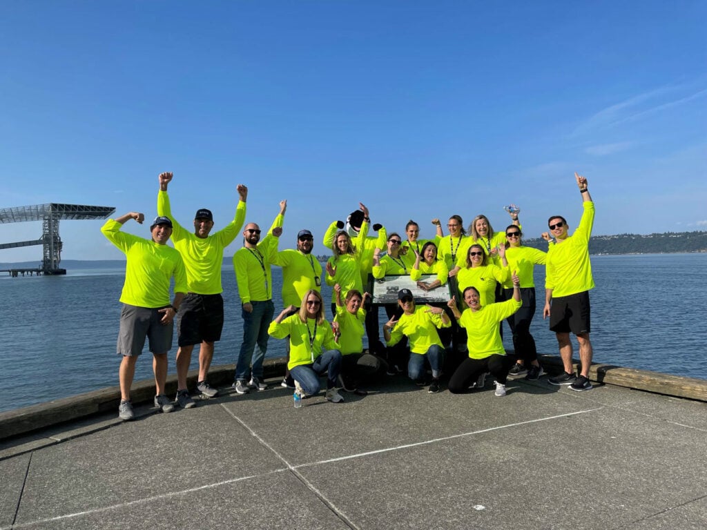 Brightly dressed group of people celebrating outdoors near water with raised arms and smiling faces.