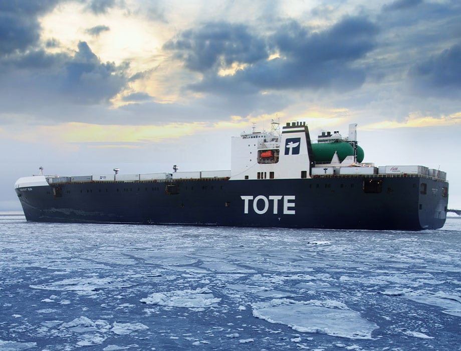 TOTE cargo ship sailing on icy water under cloudy sky.