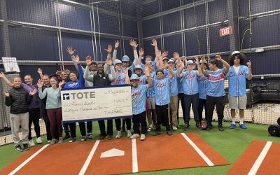 Group of people celebrating with a large check inside a sports facility.