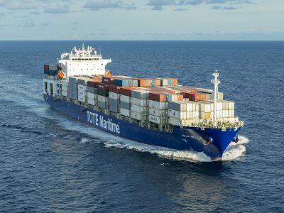 TOTE-Group-TOTE-Group-Web-Site-2.jpg Container ship sailing on the ocean with stacked cargo containers on deck.