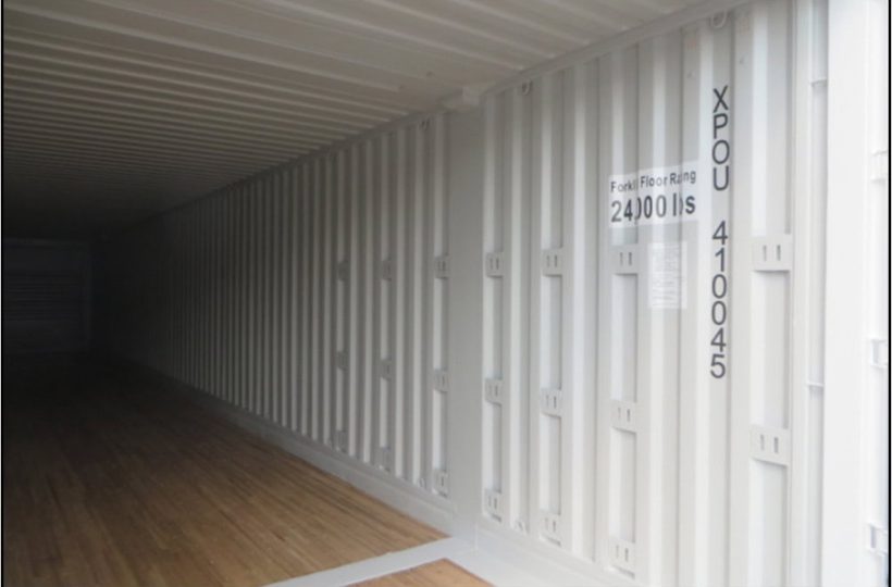 Shipping container interior with white corrugated metal walls and wooden flooring.