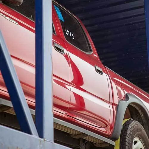 Red pickup truck parked under a roof with a blue pole in the foreground.
